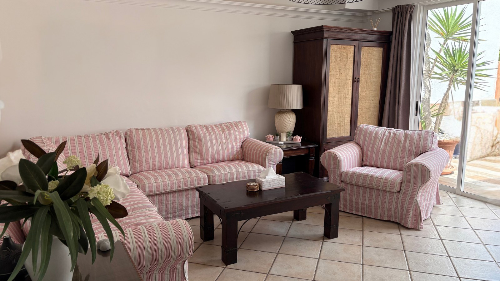 A calm living room corner with a striped sofa and armchair, a dark wood coffee table and daylight from a patio door
